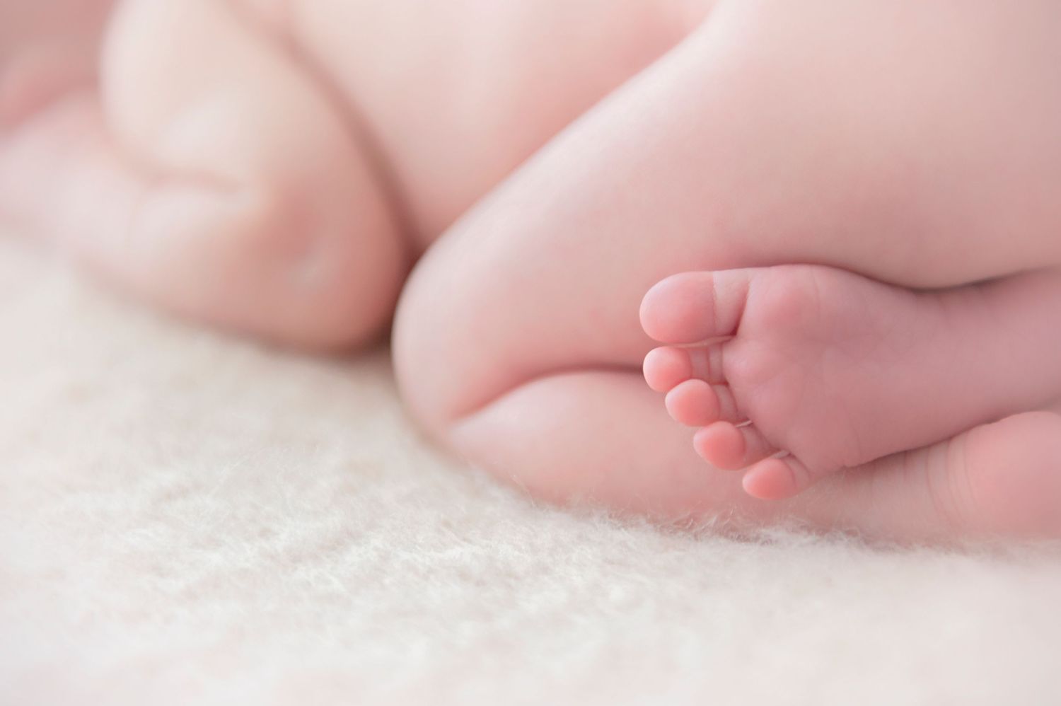 Close-up of a newborn baby's tiny foot against soft pink background.
