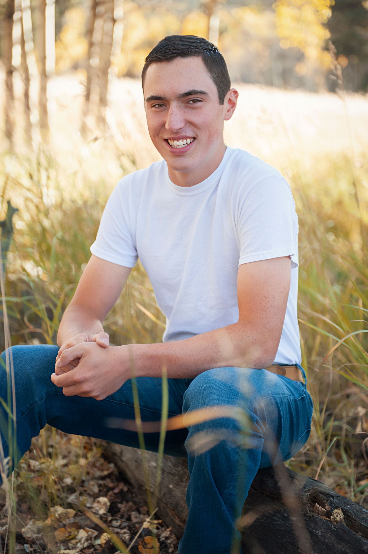 Person in white t-shirt sitting outdoors in casual pose with jeans among tall grass.