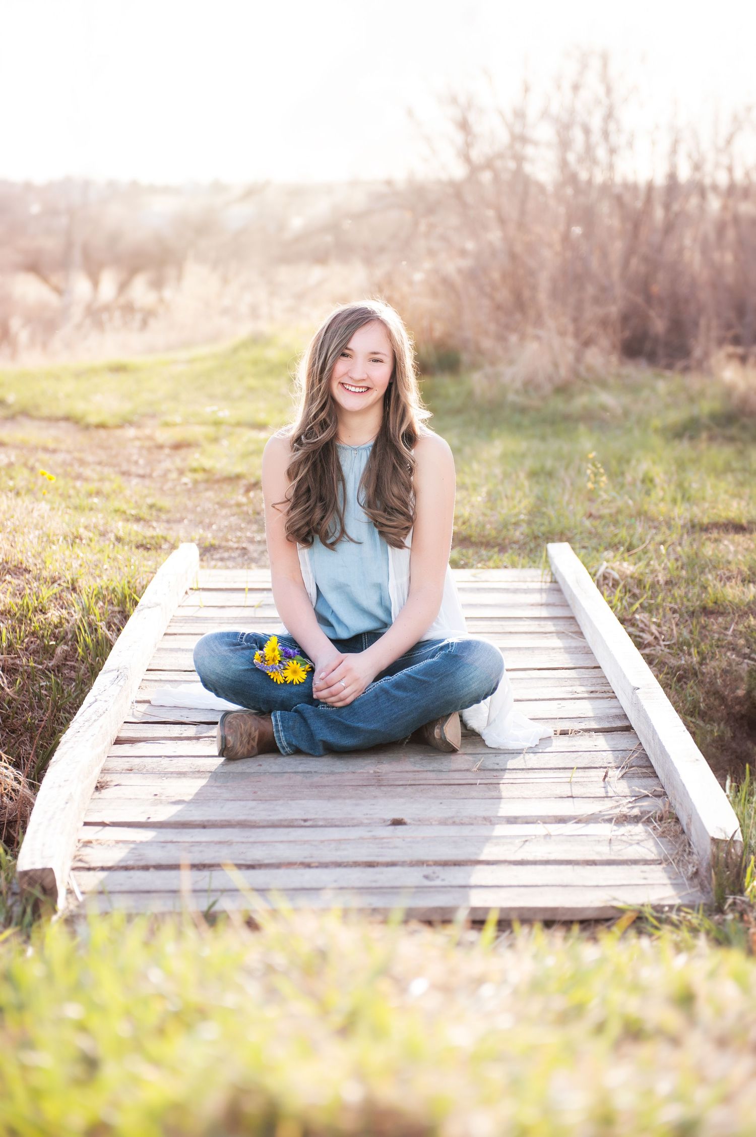 Portrait of person sitting cross-legged on wooden boardwalk in casual attire during golden hour.