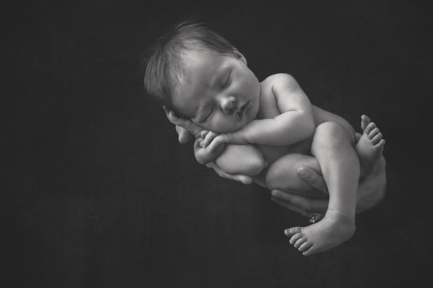 Dramatic black and white studio portrait of sleeping newborn in side-lying pose.