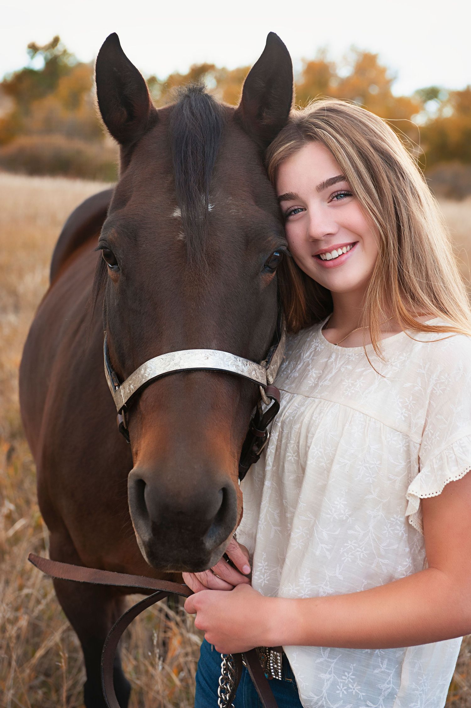 Person in white ruffled blouse poses with dark brown horse in golden field.
