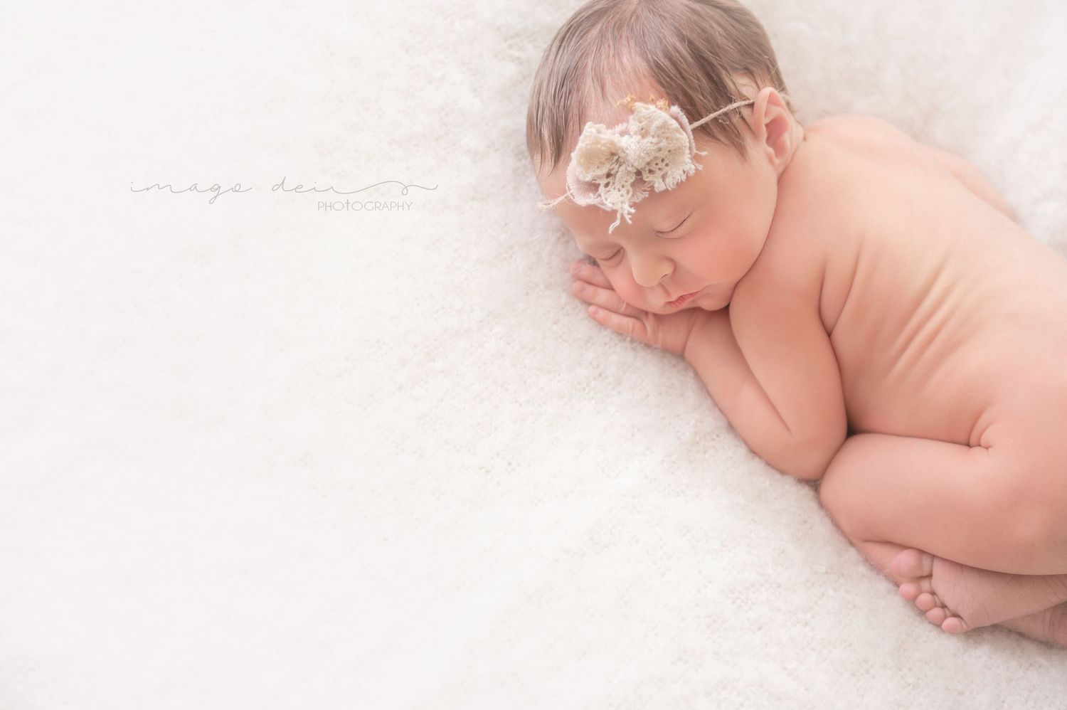 Gentle newborn pose with floral headpiece against soft white background.