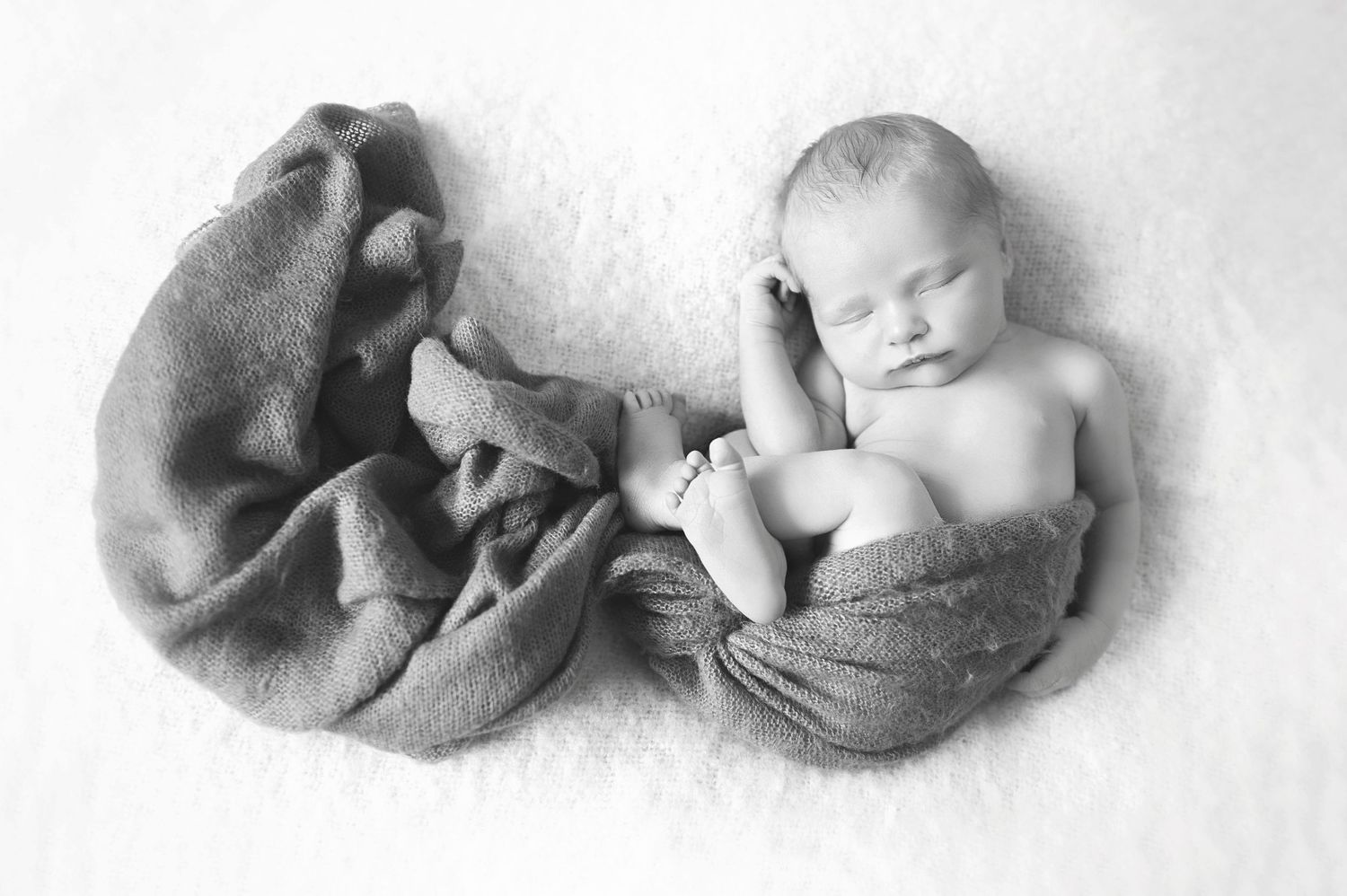 Black and white portrait of sleeping newborn wrapped in soft textile.