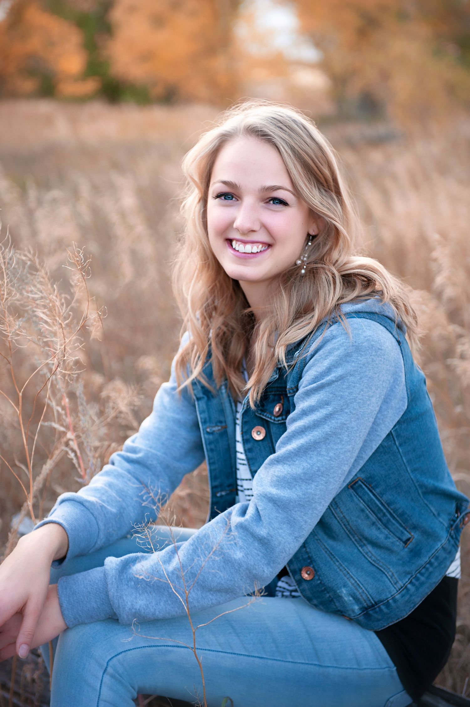 Casual outdoor portrait featuring someone in denim sitting among tall golden grass.