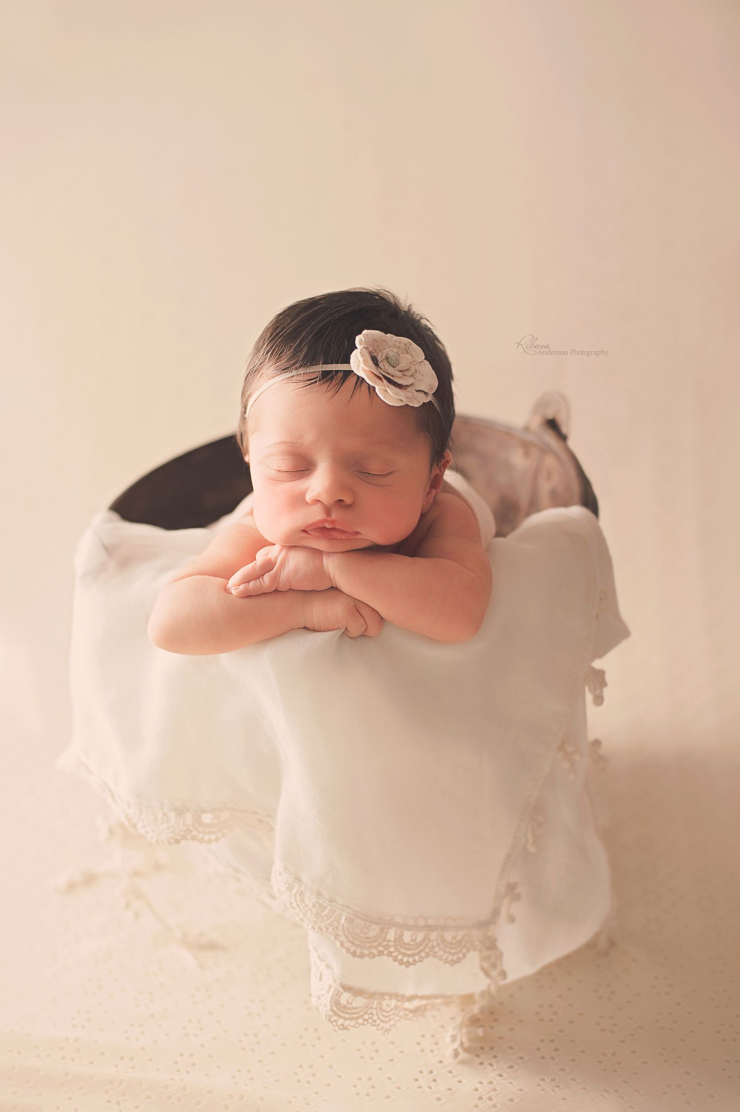 Sweet newborn sleeping on white lace blanket with bow headband in dreamy lighting.