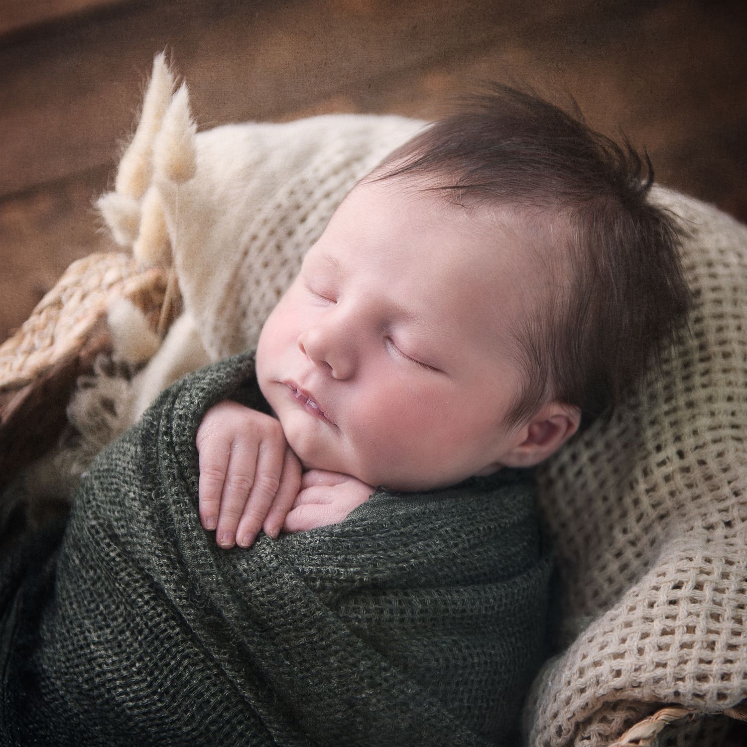 Cozy newborn portrait with baby wrapped in green swaddle and cream knit blanket.