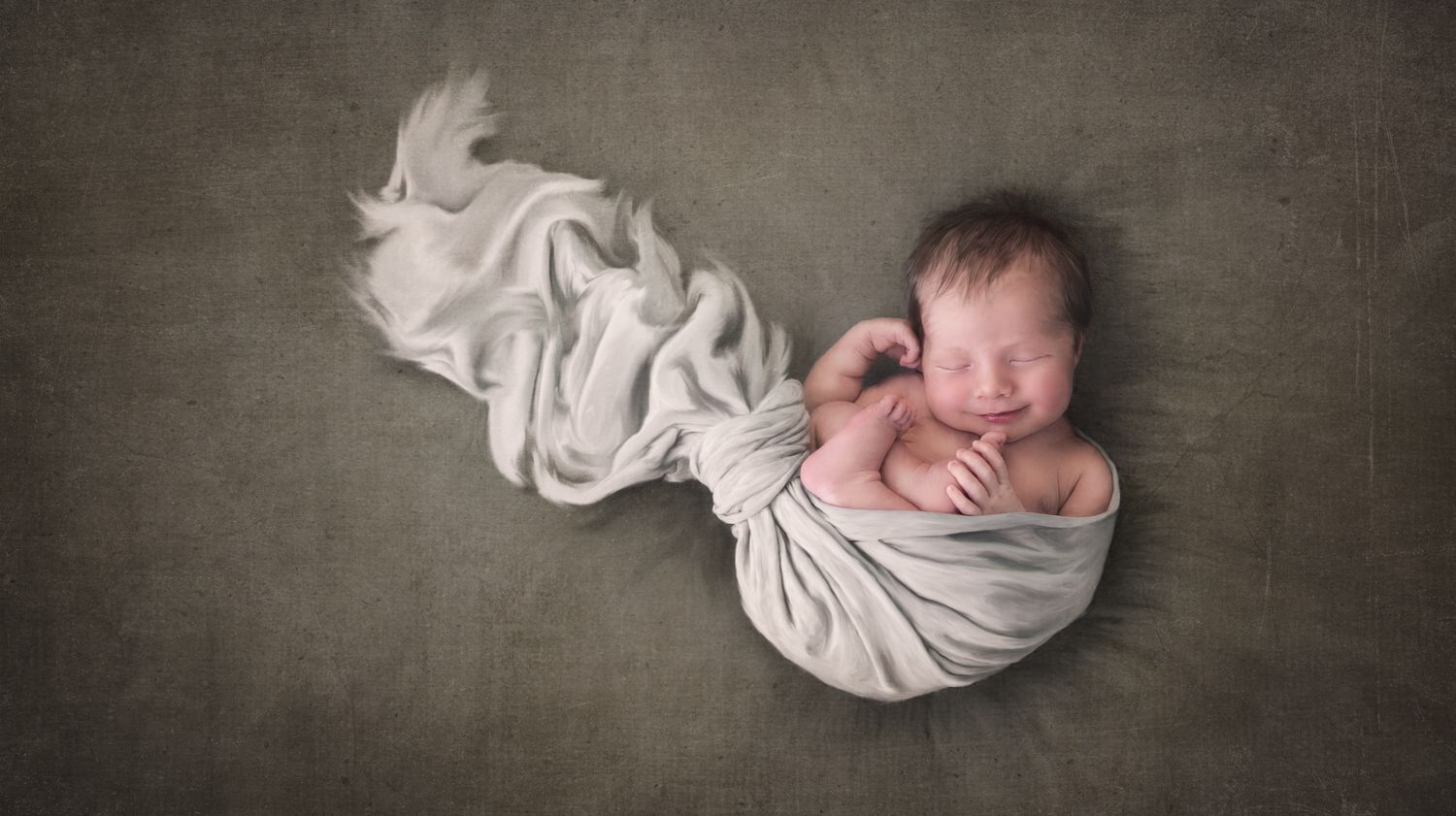 Artistic portrait of sleeping newborn swaddled in white fabric against grey backdrop.