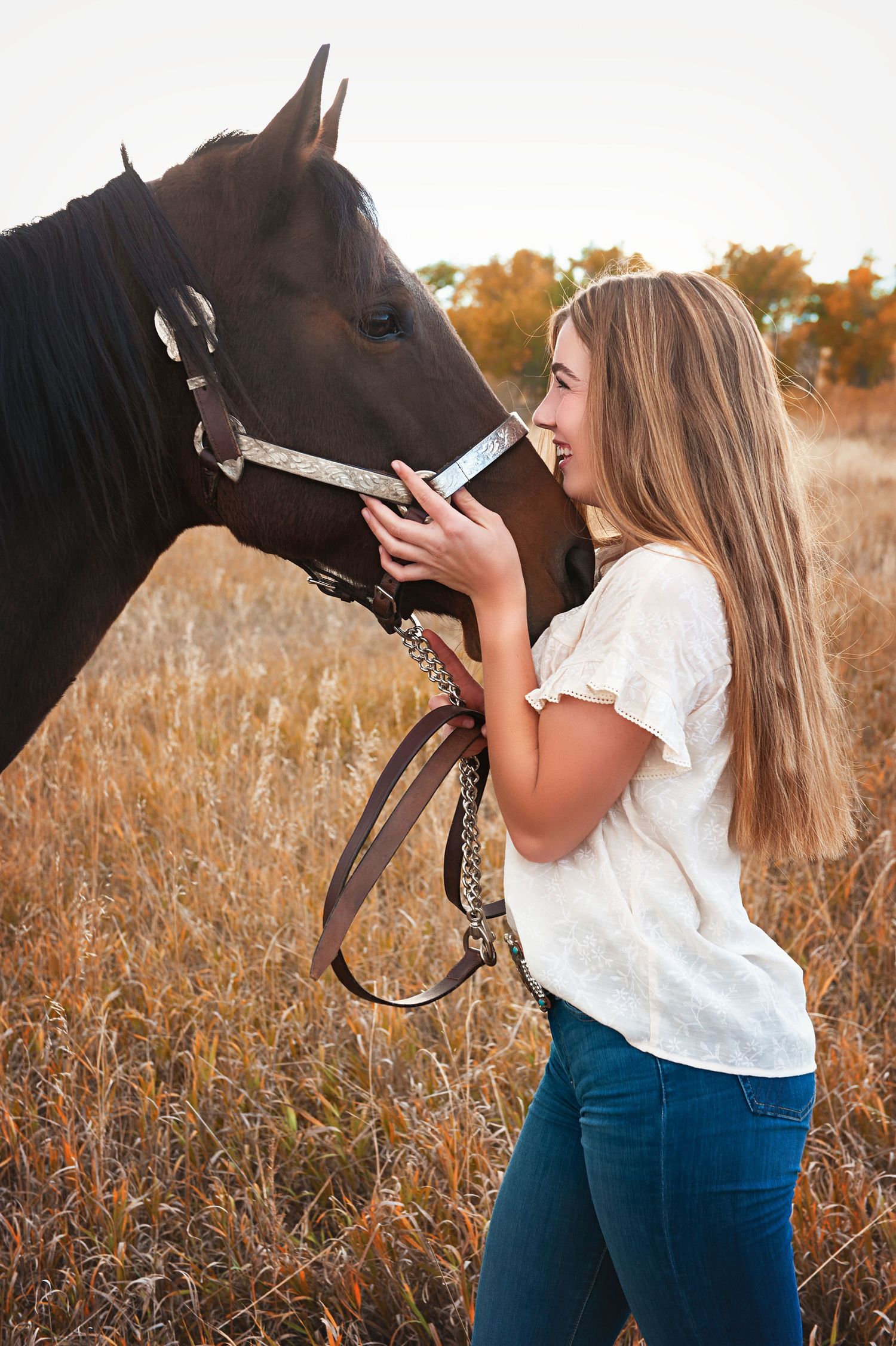 Person in white top bonding with dark brown horse in autumn field at sunset.