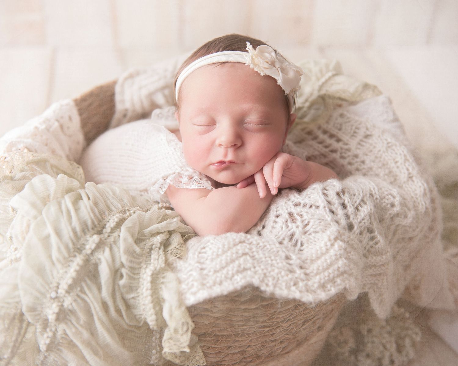 Newborn sleeping in rustic basket wrapped in cream colored lace and knits.