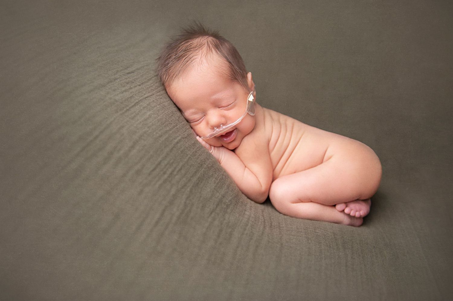 Sleeping newborn curled up on soft gray textured backdrop in natural lighting.