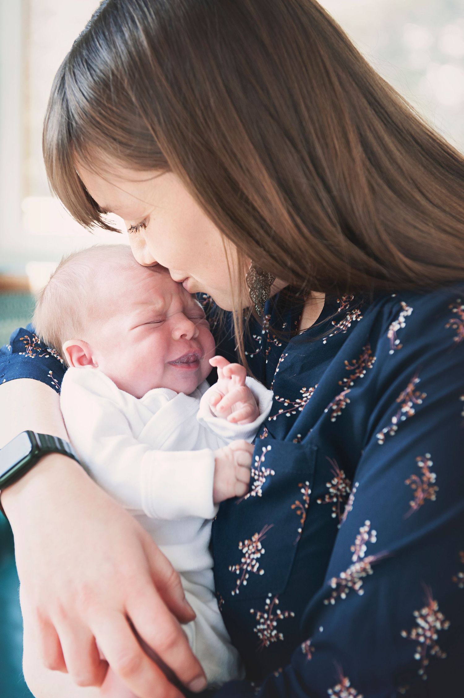 Tender moment between parent and newborn baby in white onesie against floral print dress.