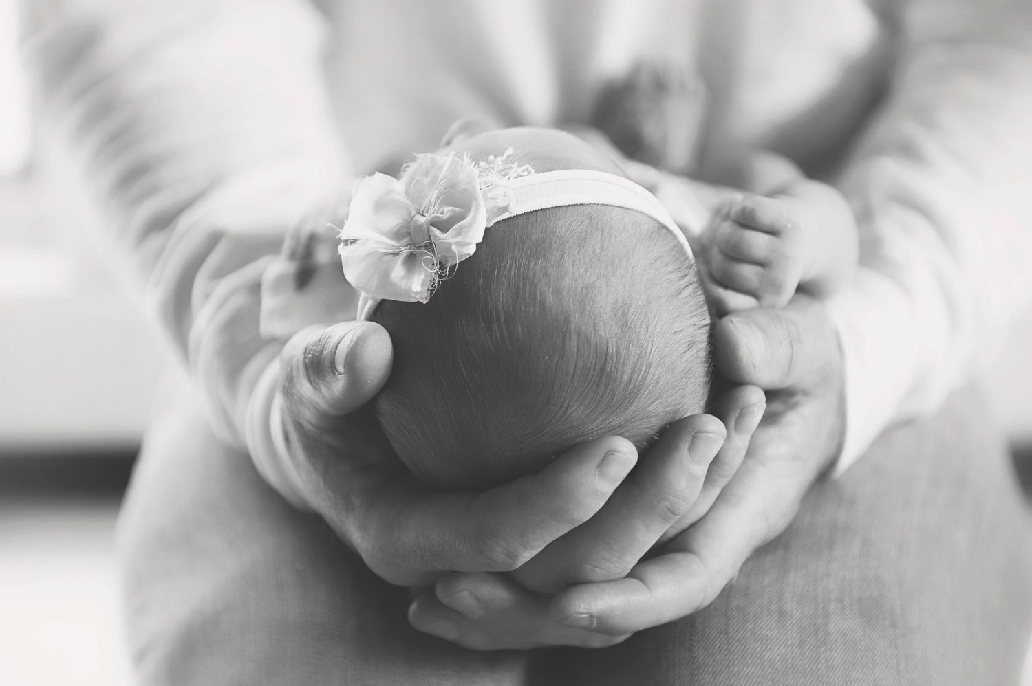 Black and white image of small baby with flower headband cradled in hands.