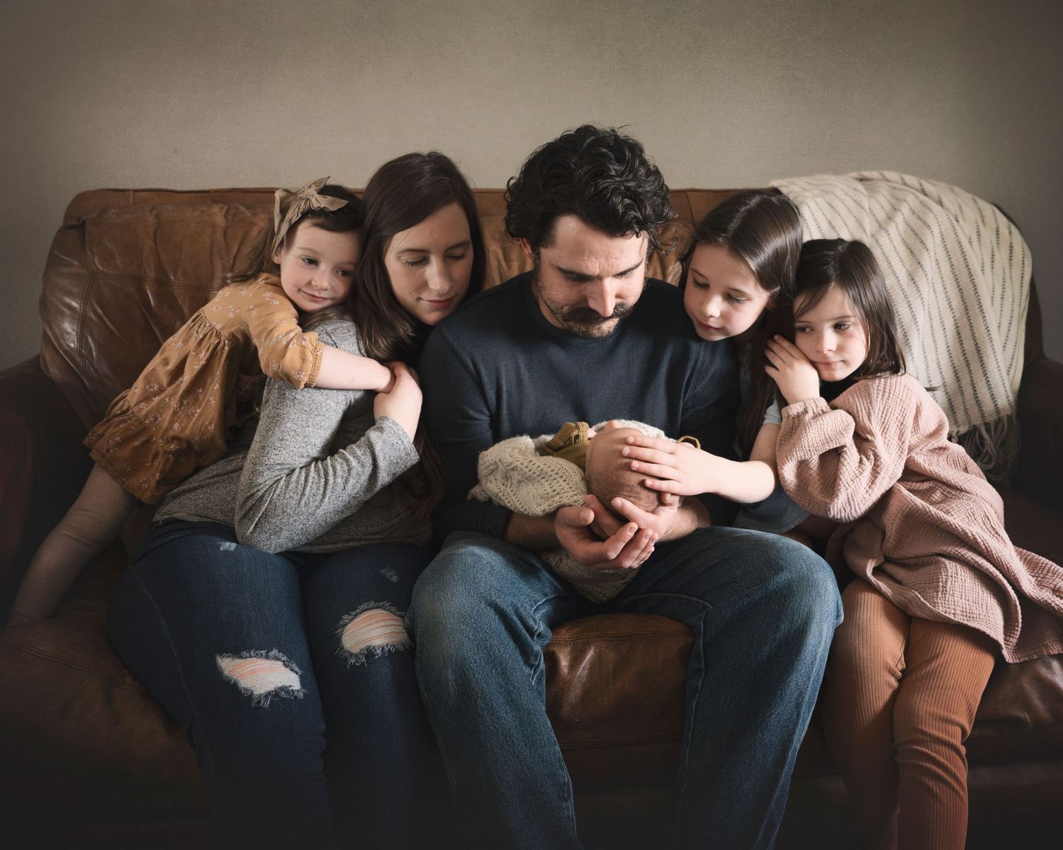 A cozy family moment on a brown leather couch with a new baby.