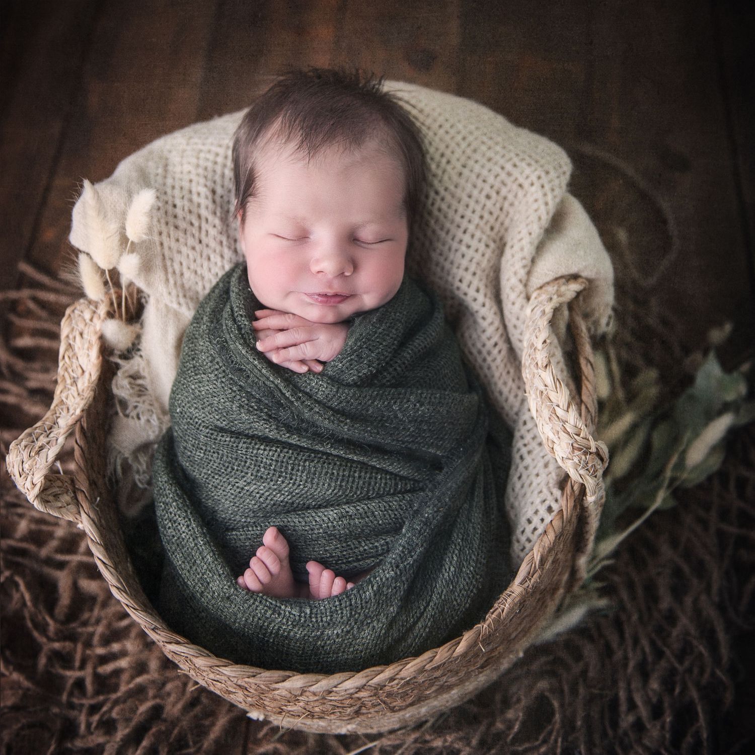 Professional newborn portrait with baby wrapped in green swaddle in rustic basket setting.