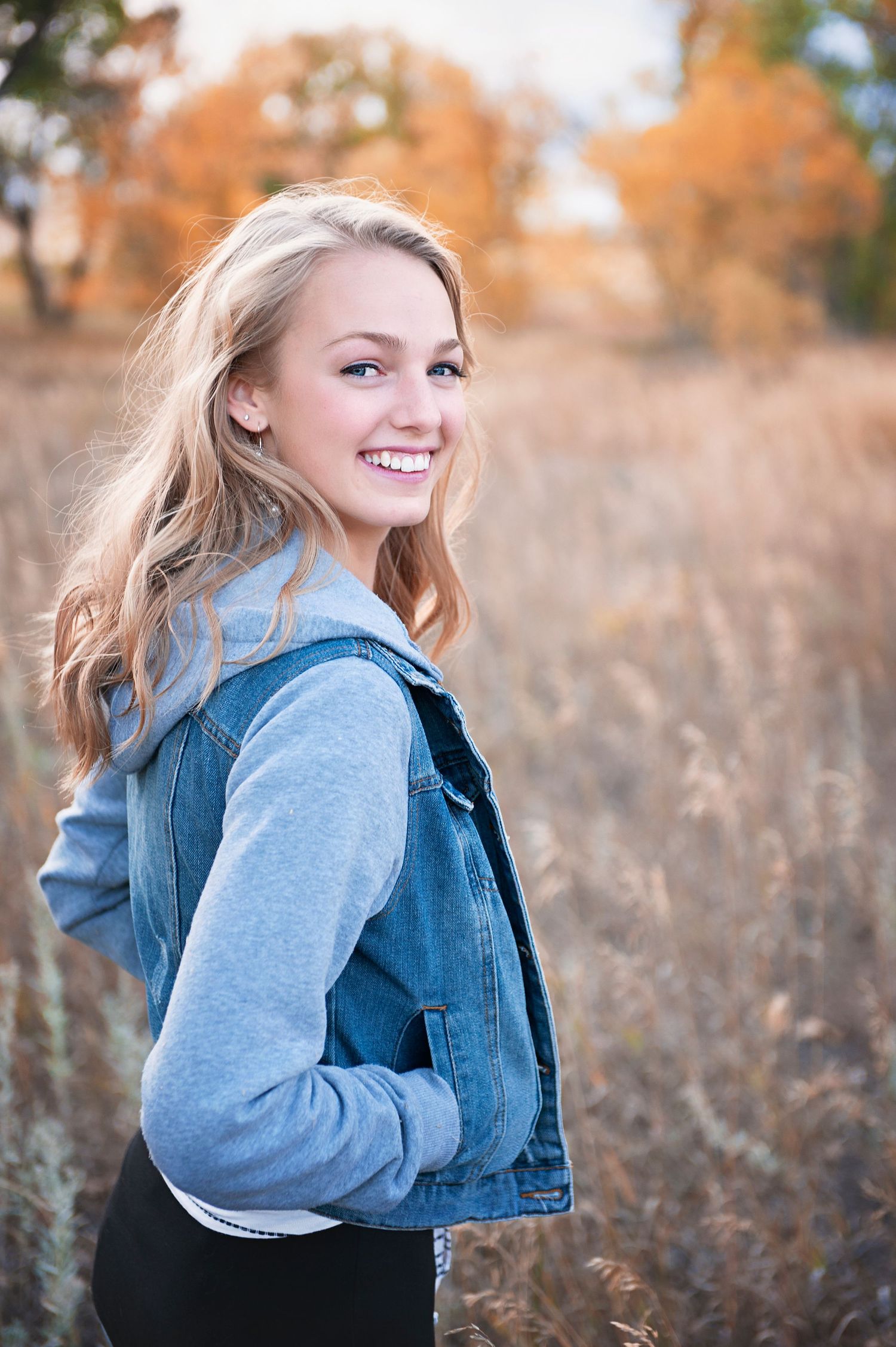 Casual portrait in denim jacket with grey sleeves against autumn field backdrop.