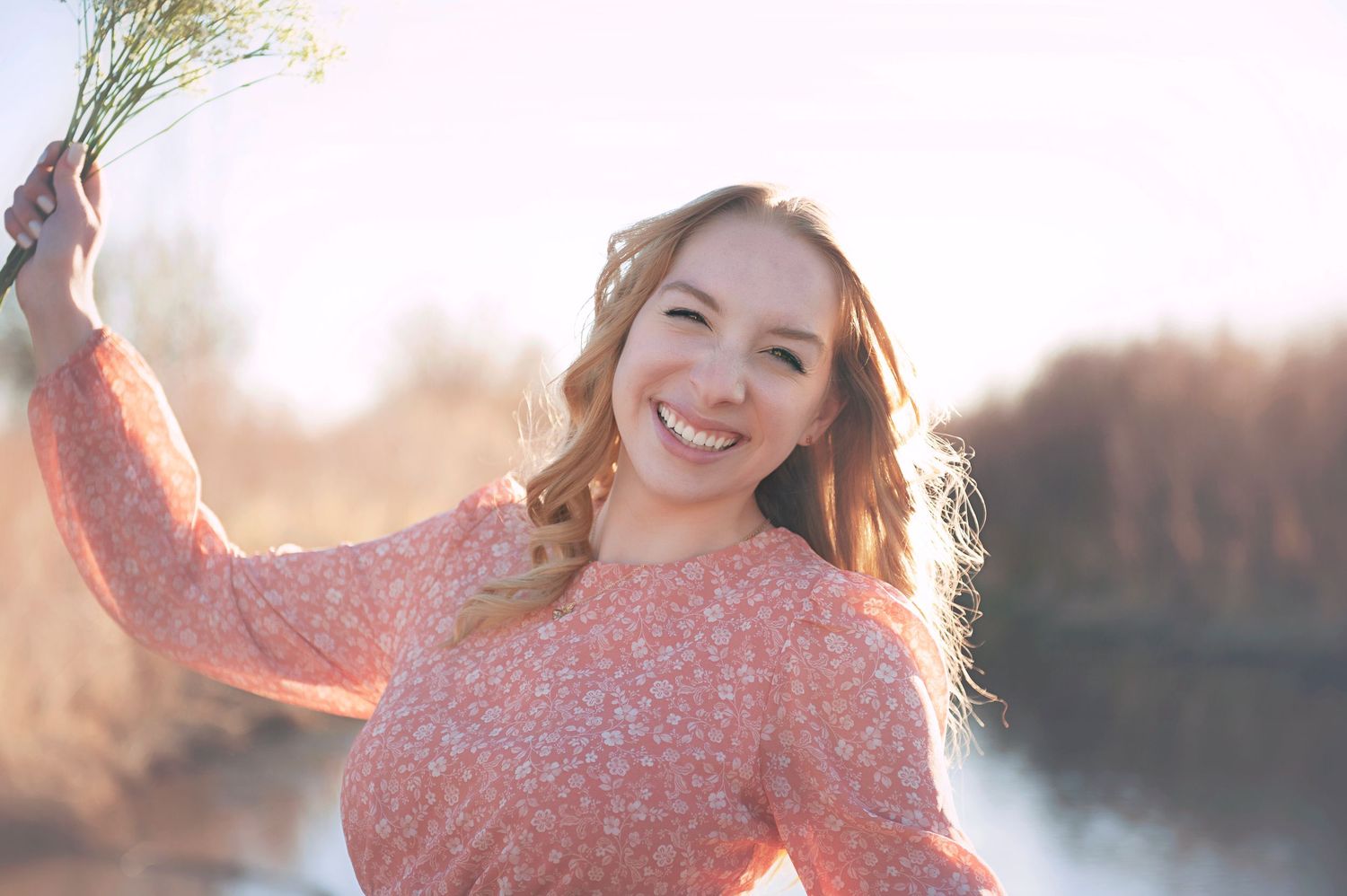A joyful moment captured in soft sunlight near a lake wearing a coral colored top.