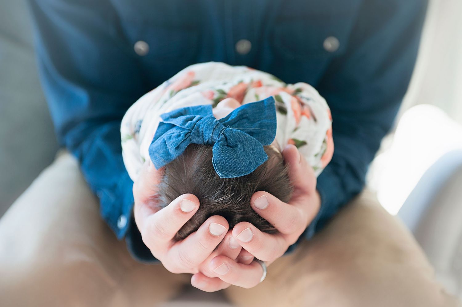 Close-up of tiny baby in floral swaddle and blue bow held in gentle hands.