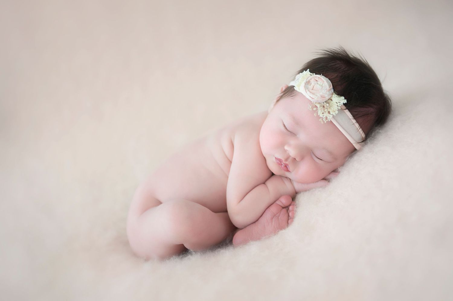 Sleeping newborn with lace headband posed on soft pink blanket in artistic portrait.