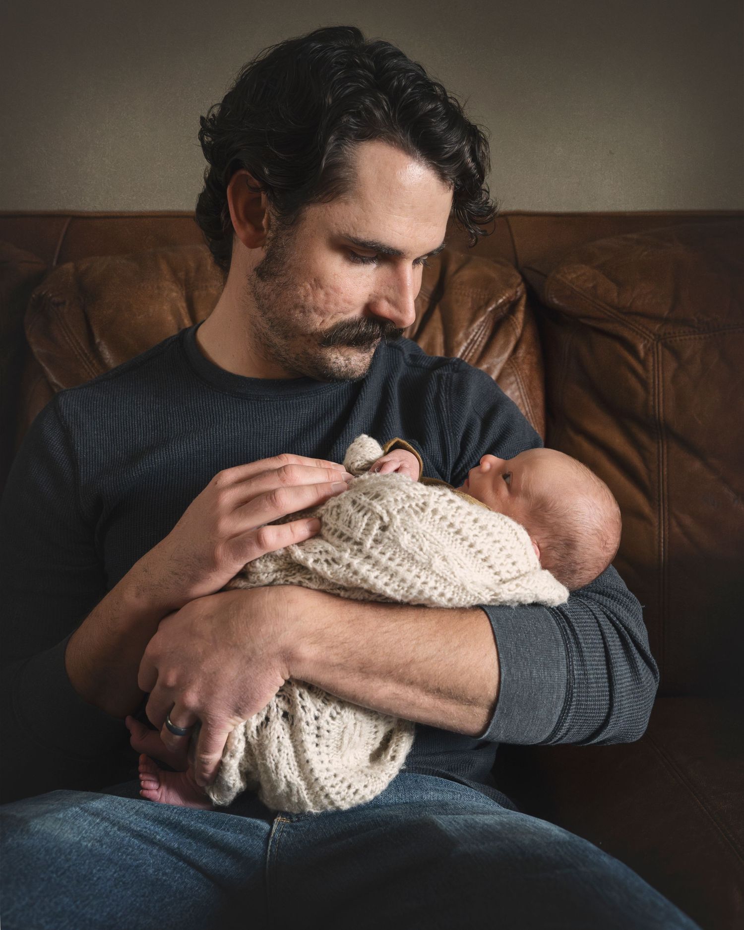 A peaceful moment showing a baby nestled in a cozy knit blanket on a leather couch.