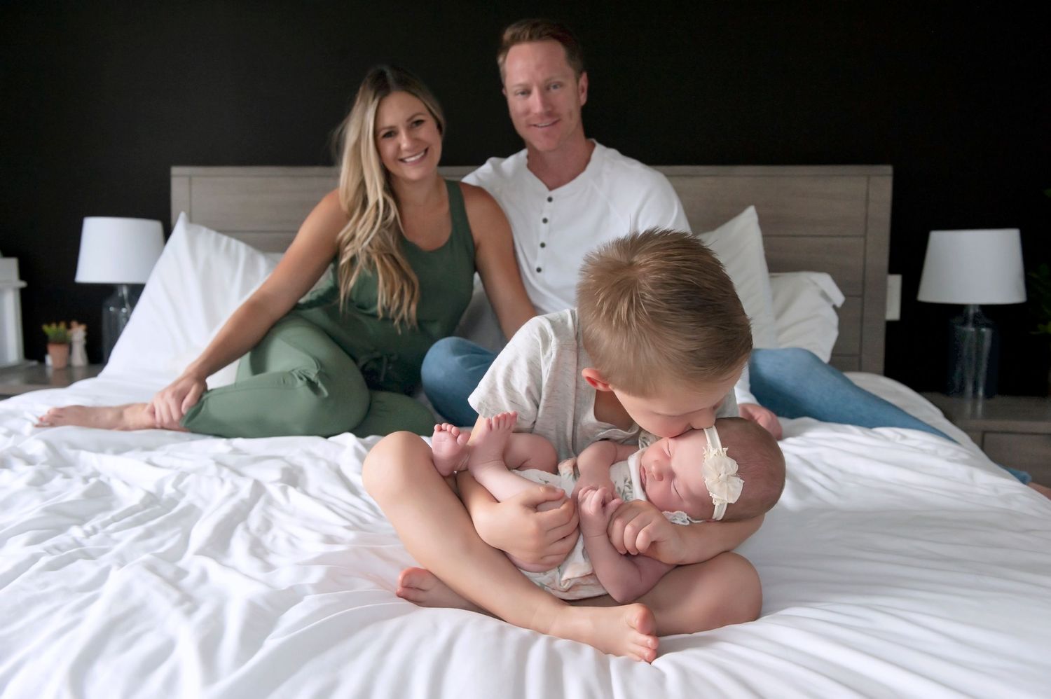 Family sharing joyful moment together on bed as older sibling bonds with newborn baby.