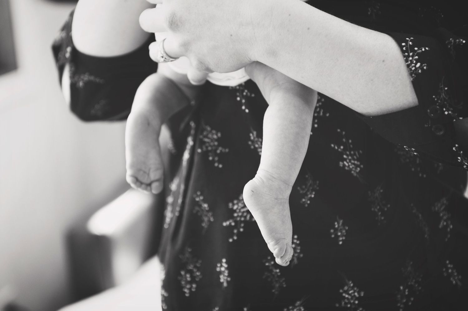 Close-up of tiny baby feet being held against dark floral patterned fabric.