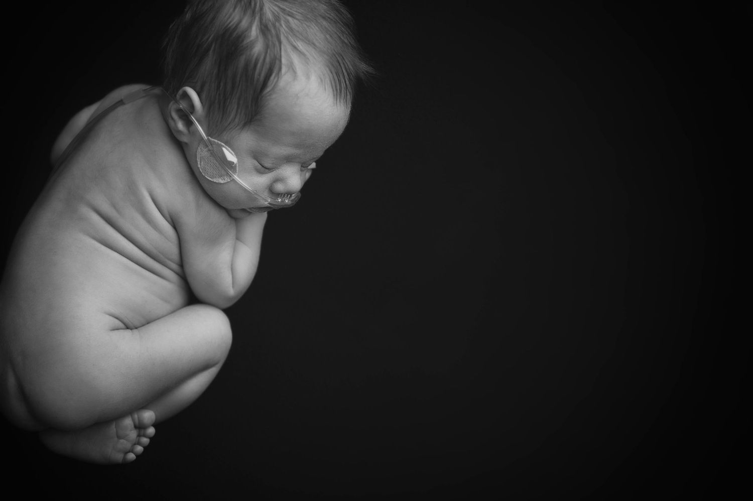 Artistic black and white side profile of newborn against dark background.