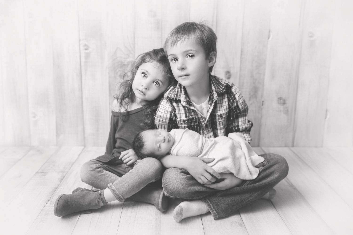 Black and white portrait of three siblings sitting together on a light floor.