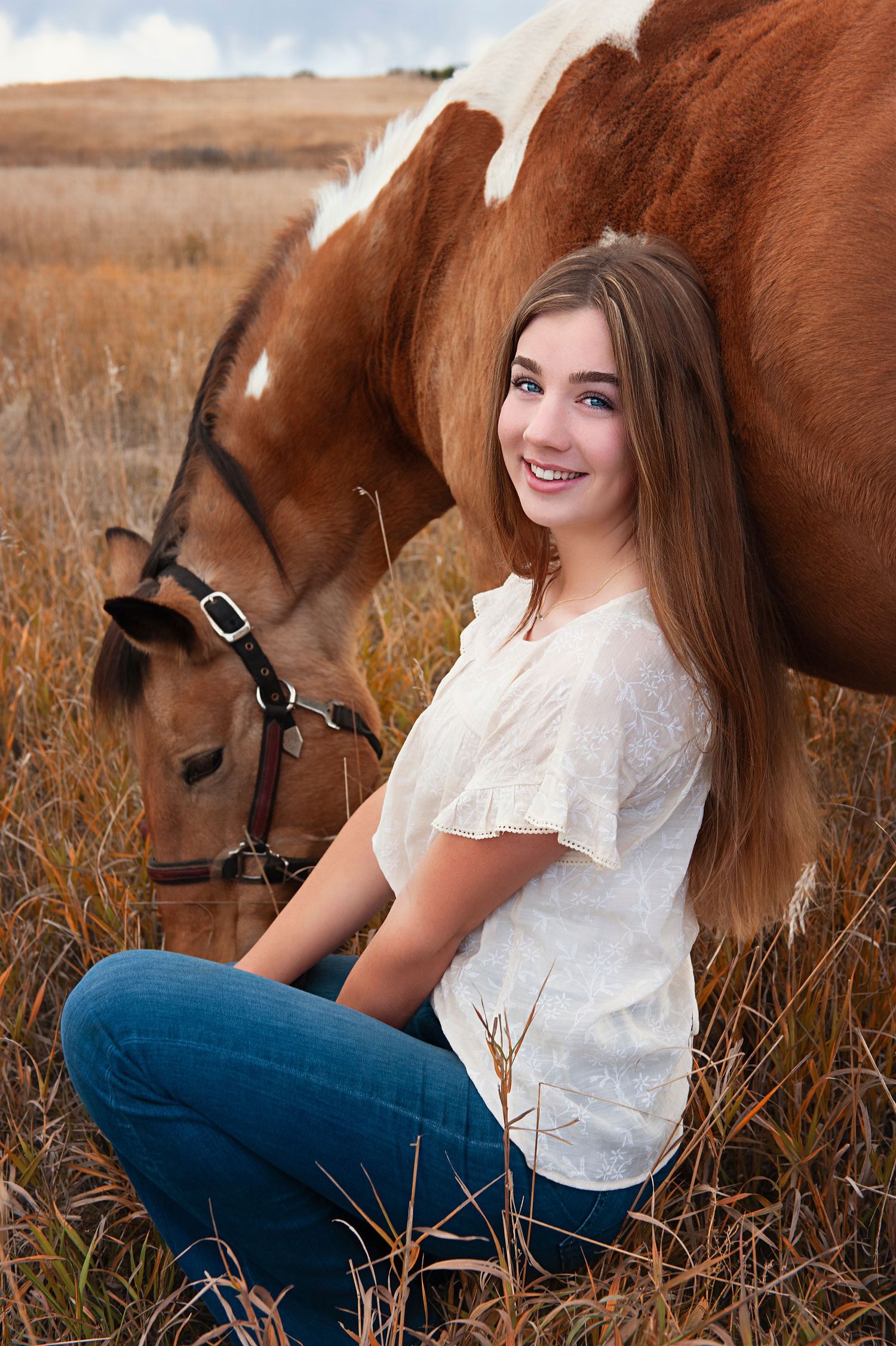 Person in white top sitting with paint horse in autumn field.
