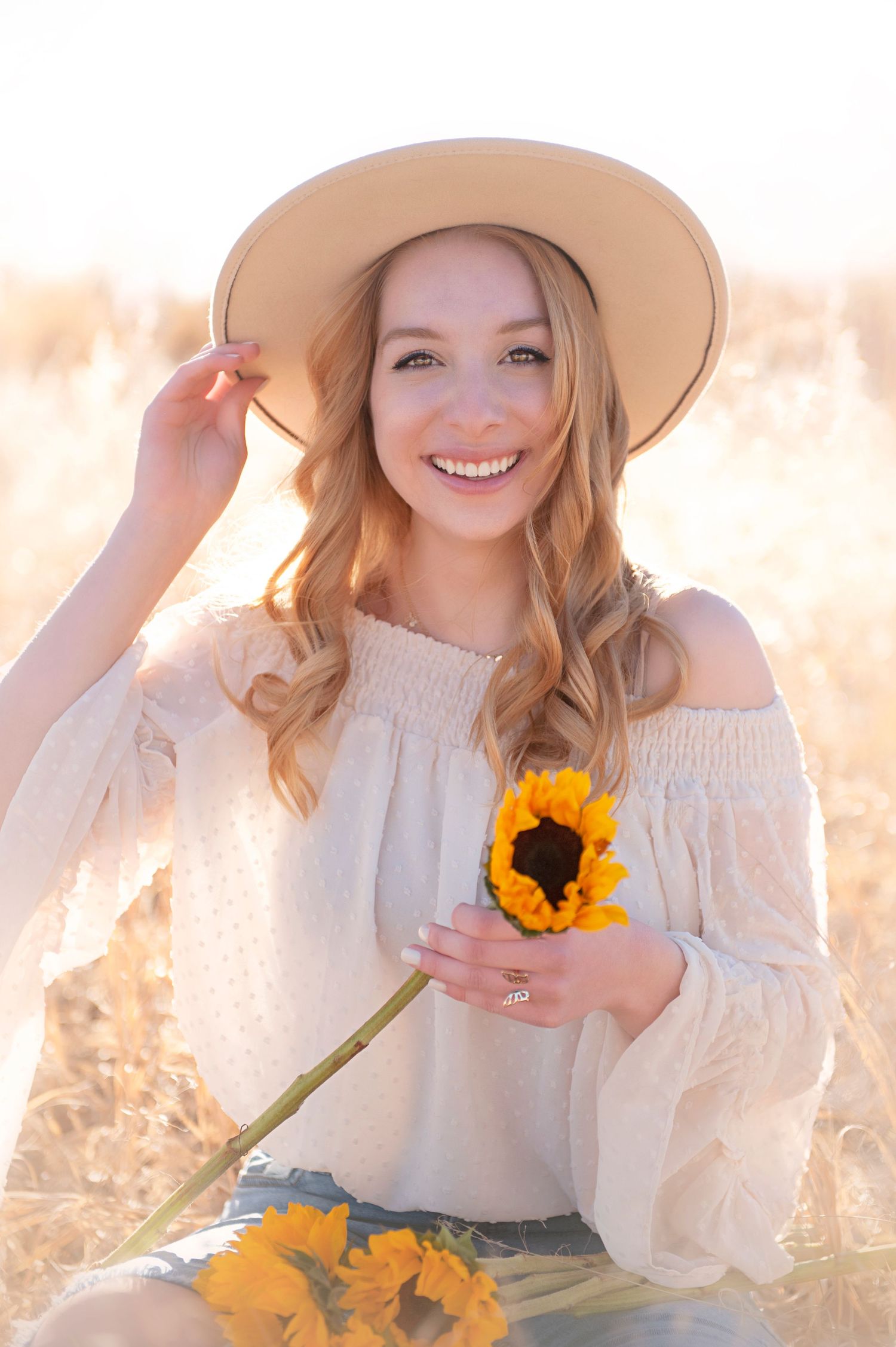 Natural light portrait with sunflower and white peasant top in golden field.