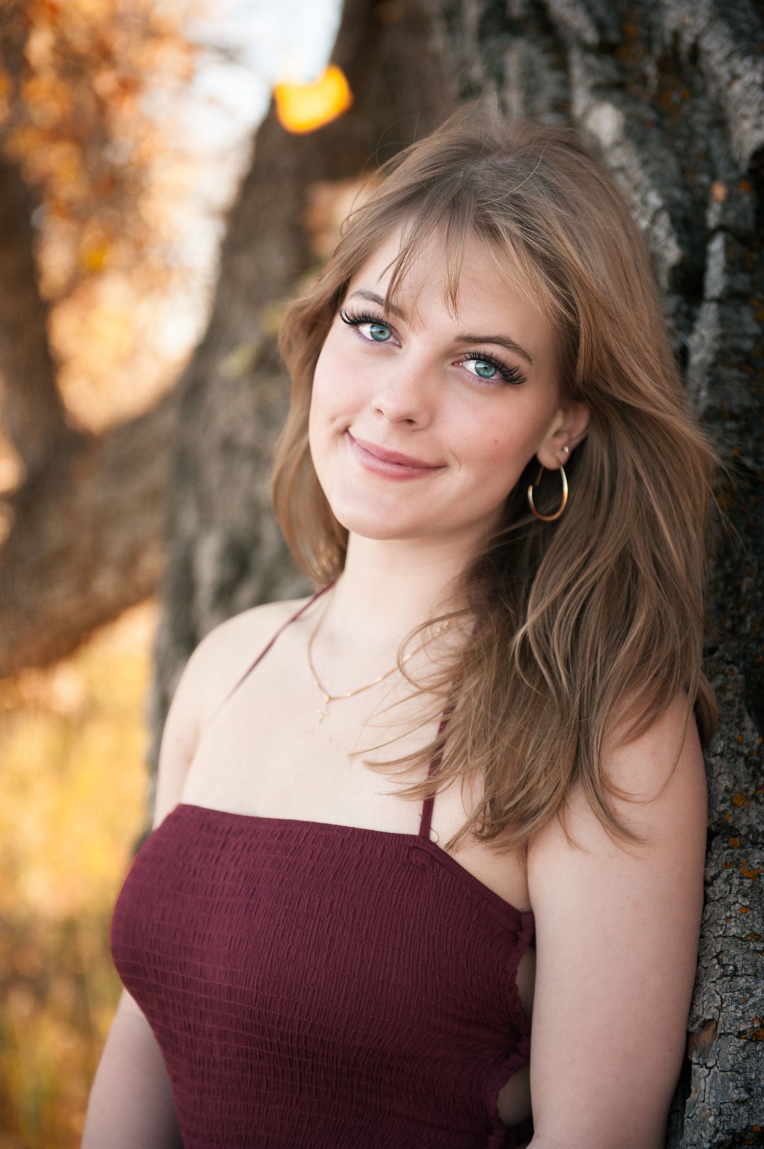 Portrait against tree trunk with warm autumn colors in background.