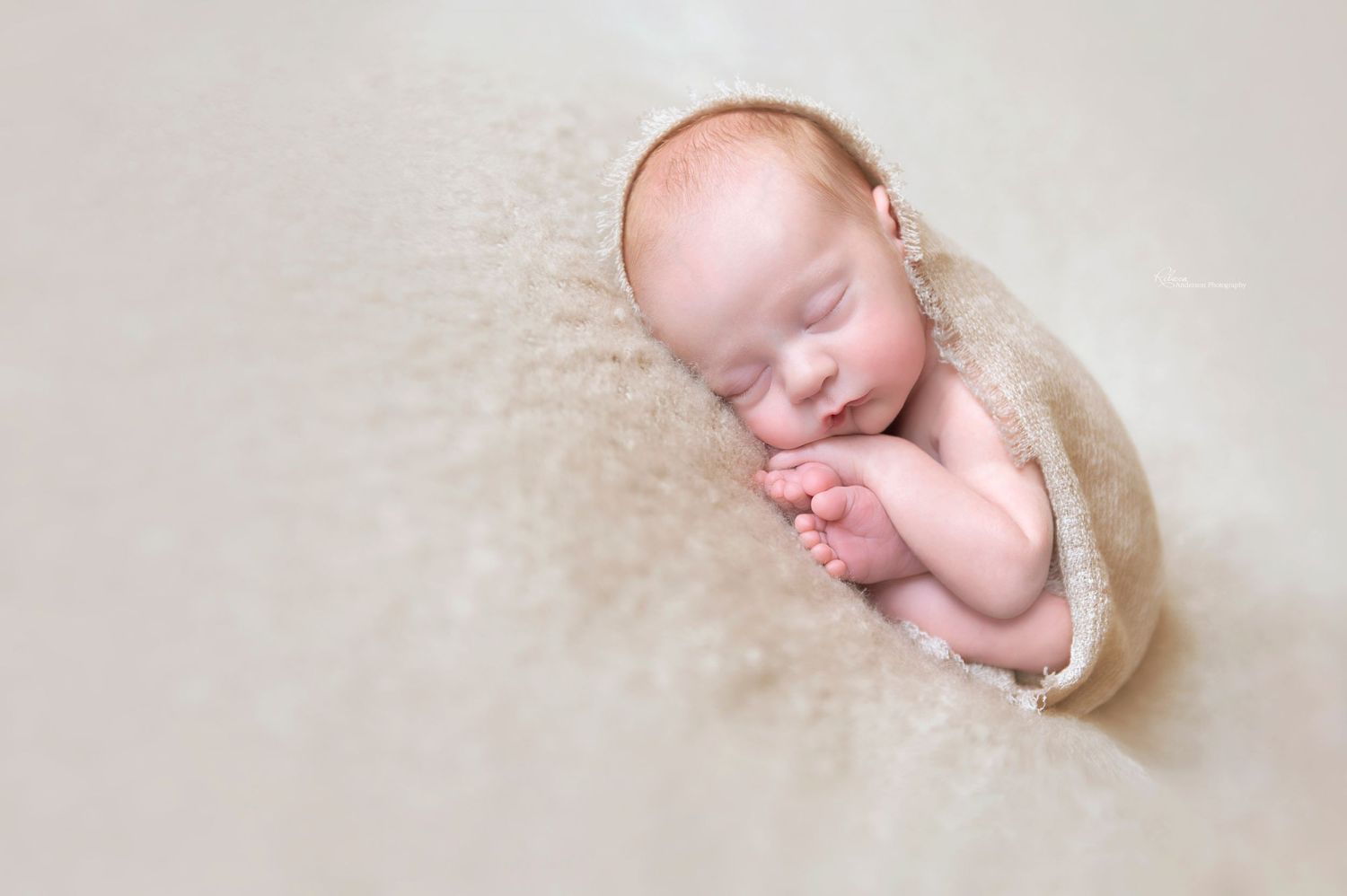 Peaceful newborn wrapped in cream fabric rests on textured beige background during photo session.