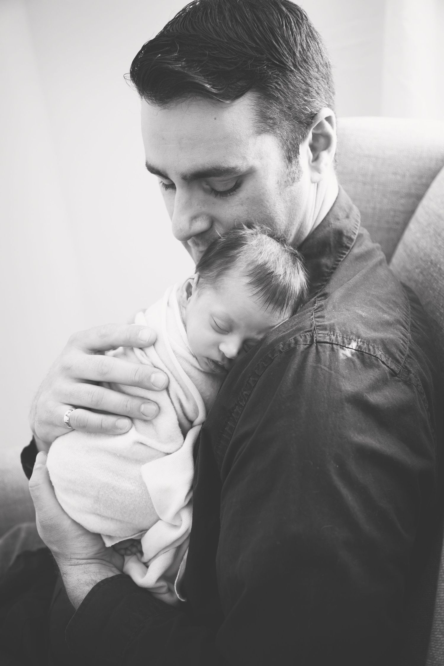 Black and white portrait of parent tenderly holding sleeping infant against shoulder.