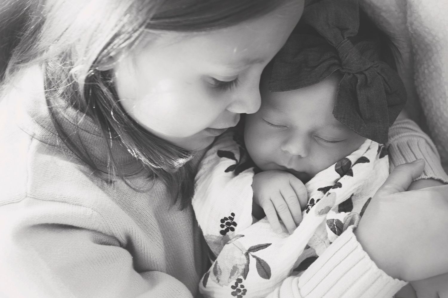 Black and white portrait of children in a close embrace with floral swaddle.