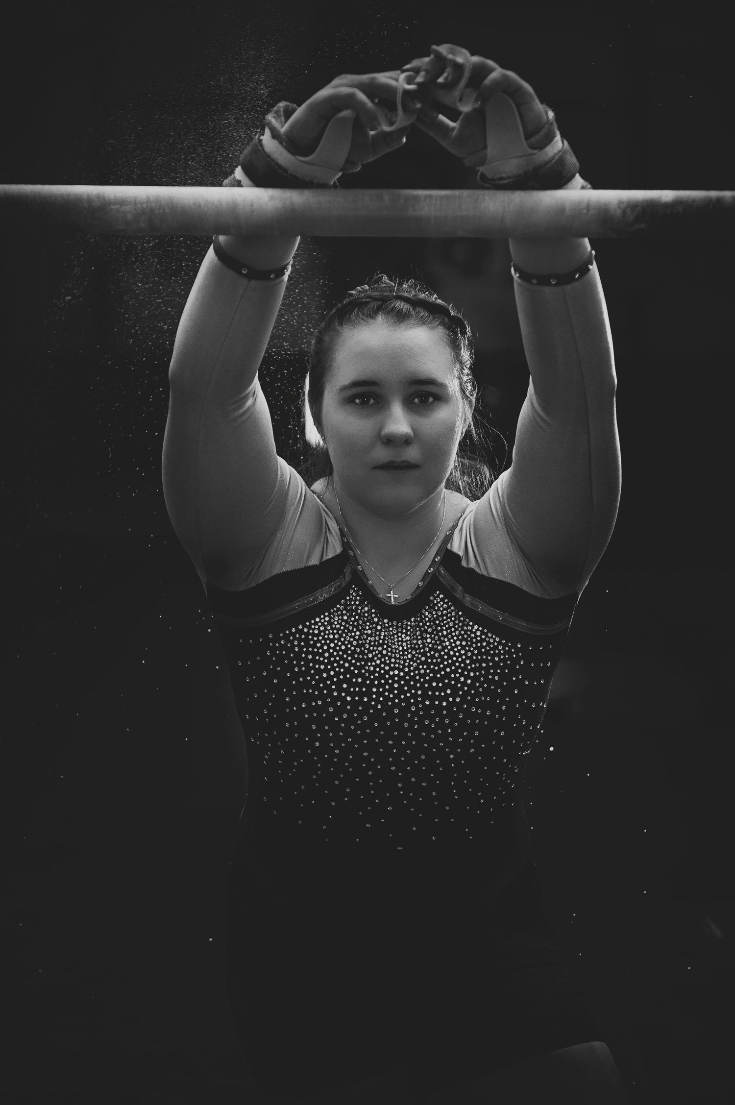 Gymnast in sparkling leotard performing on uneven bars in dramatic black and white lighting.