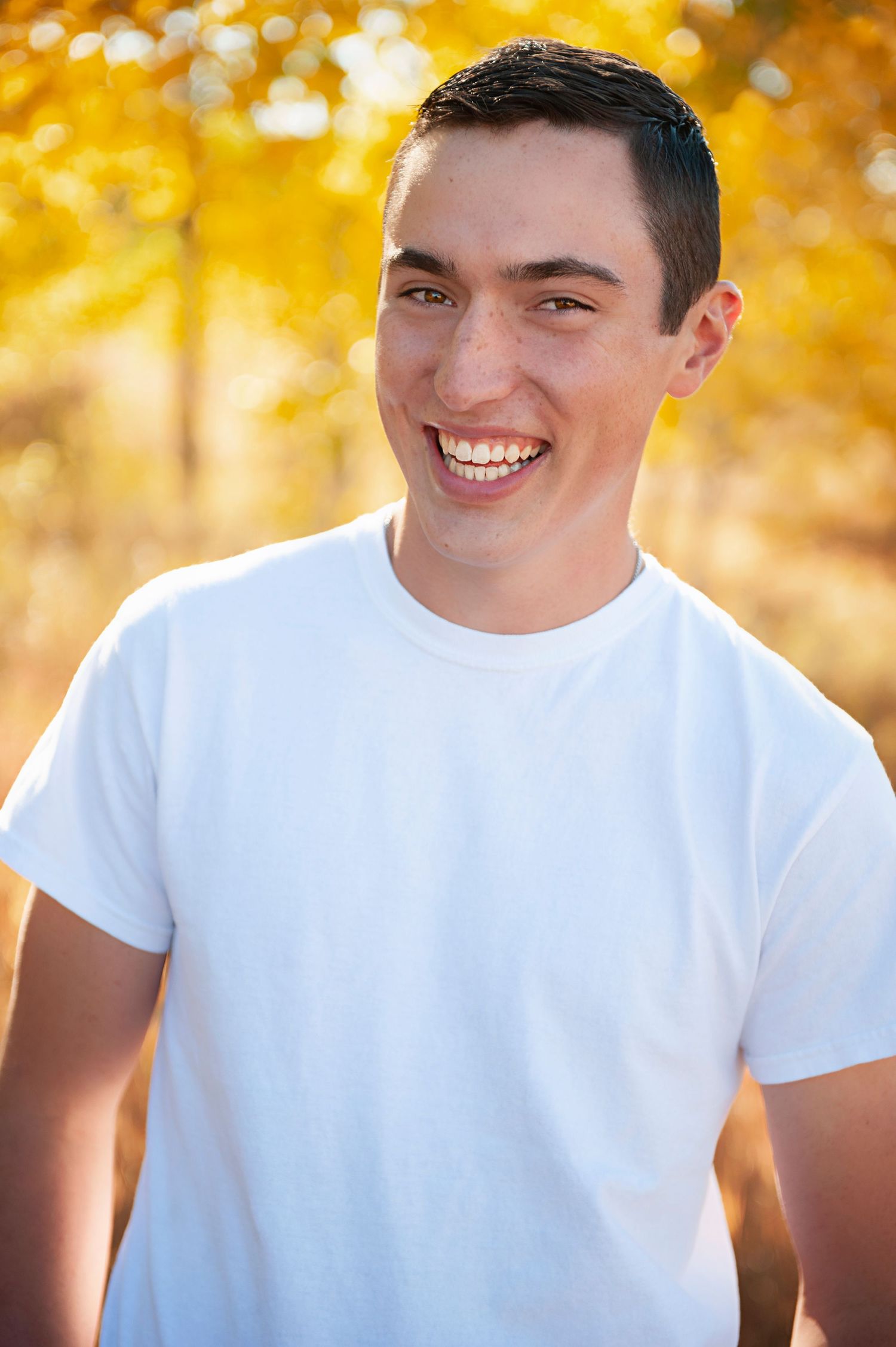 Portrait of a young person wearing a white t-shirt smiling against a golden autumn background.