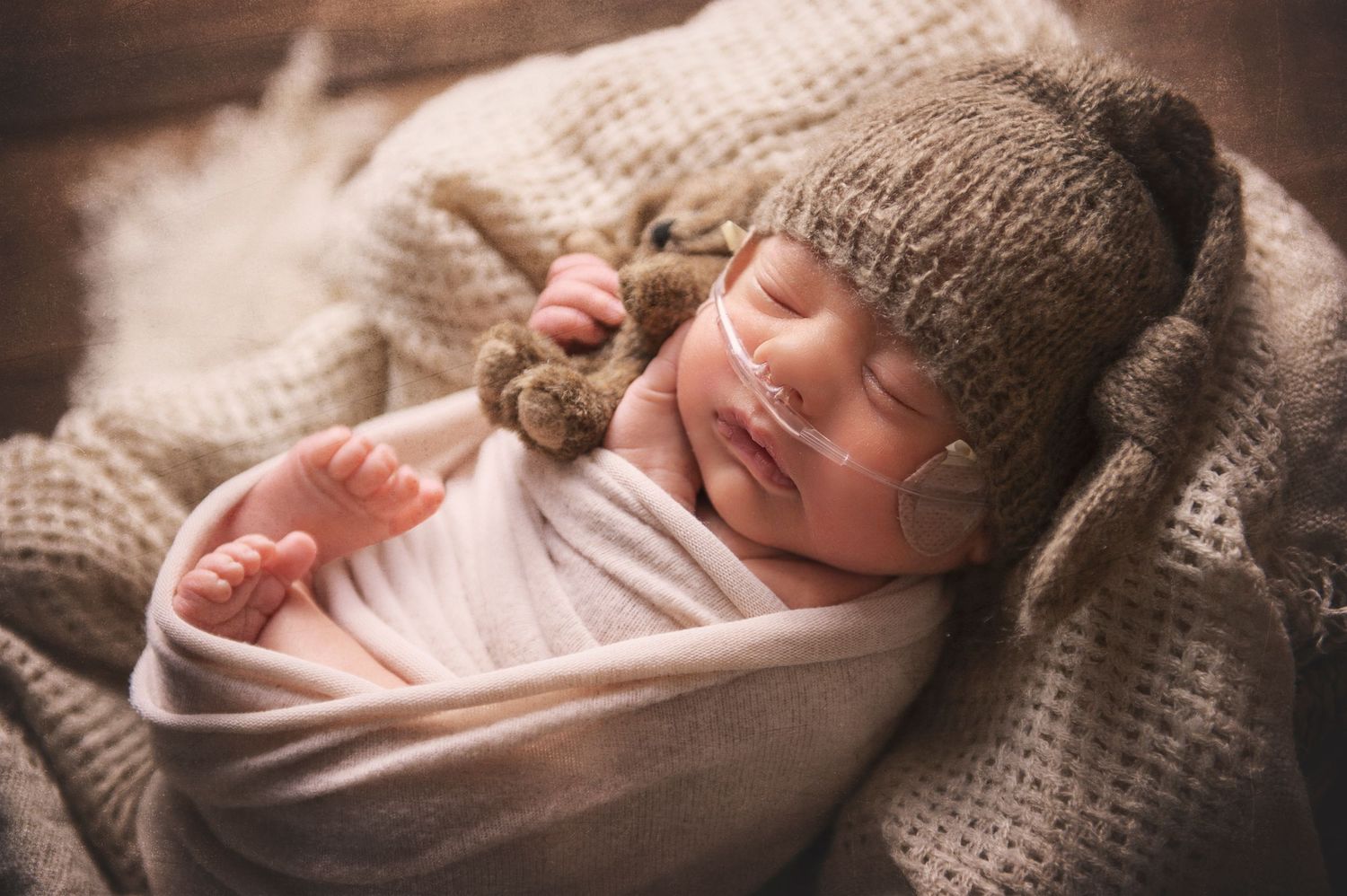 Sleeping newborn wearing cozy knit hat swaddled in white fabric on textured blanket.