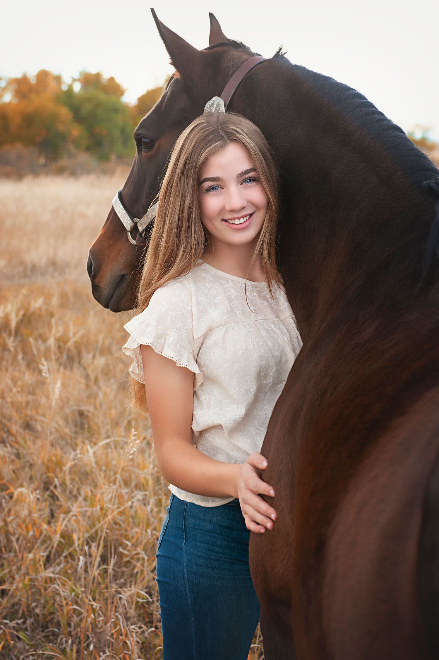 Person in white top stands next to dark brown horse in autumn meadow.