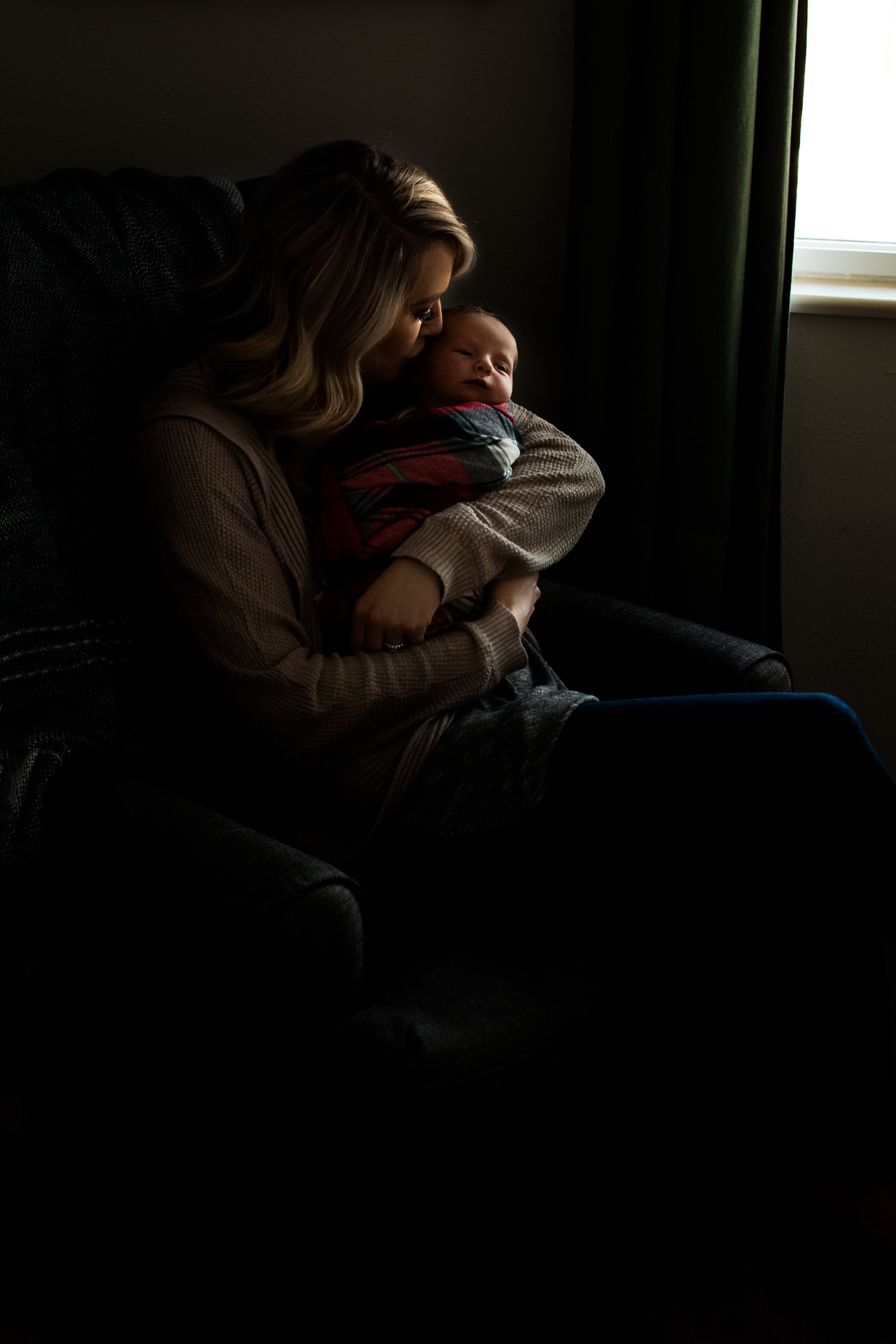 Silhouetted figure holding infant by window in atmospheric lighting.