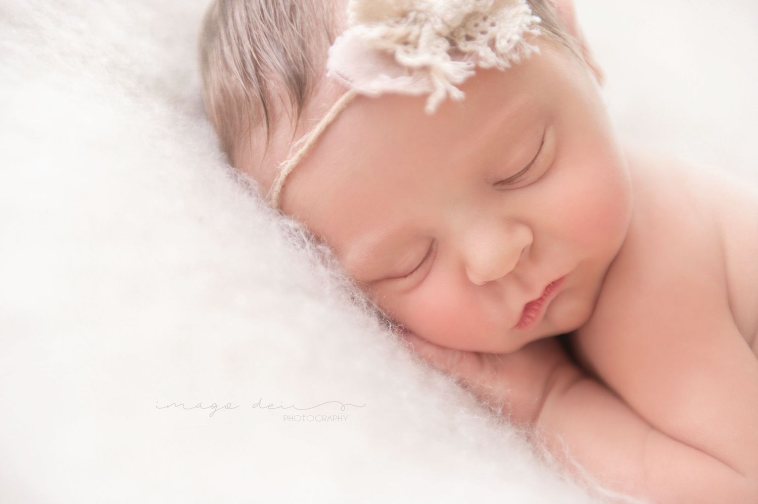 Peaceful sleeping newborn portrait with lace hair accessory on white.