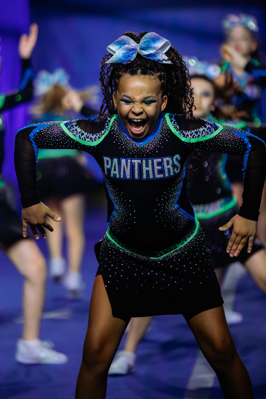 Young Panthers cheerleader performs energetically in black rhinestone uniform with neon green trim at a cheer competition.