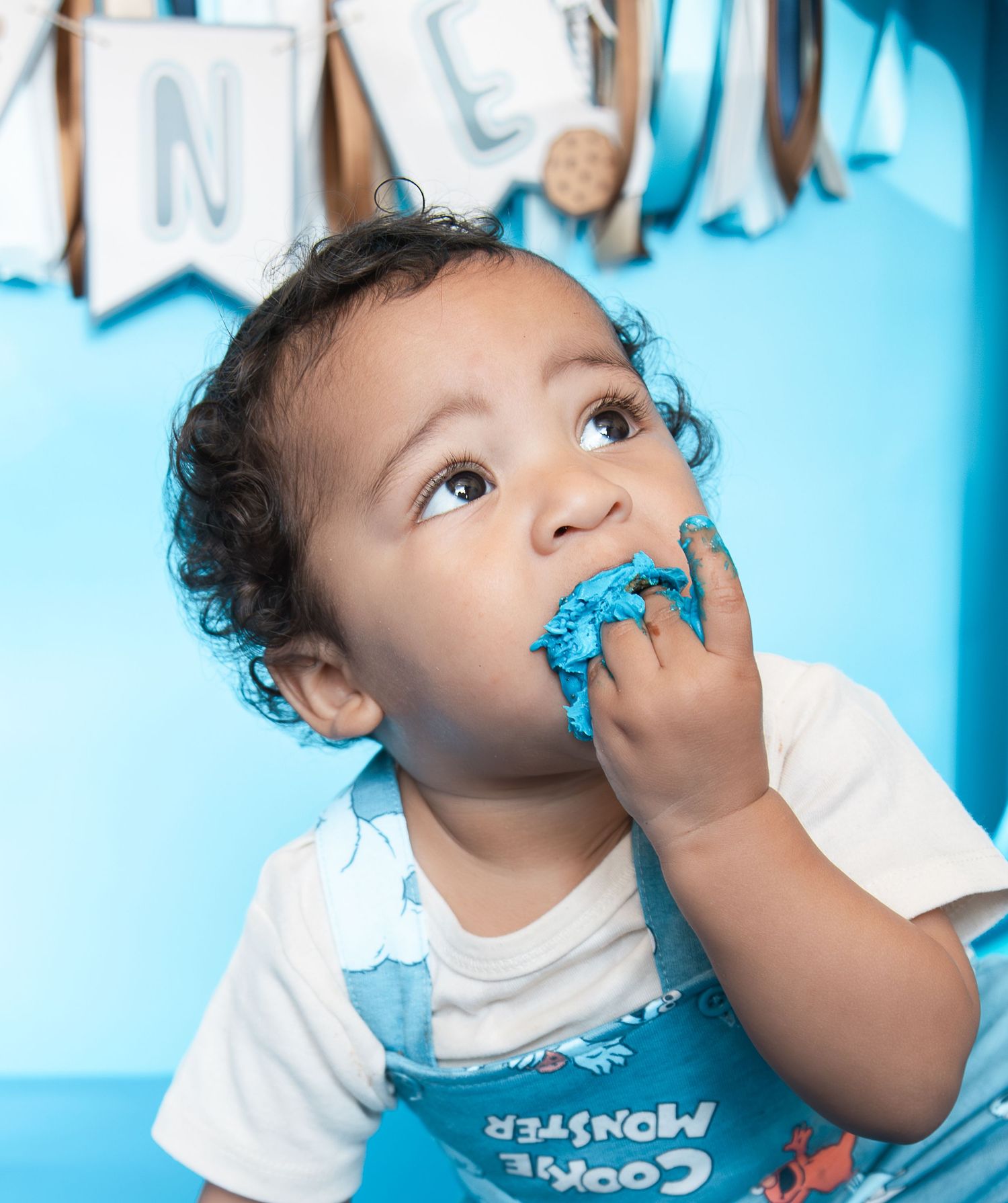 Toddler eating blue frosting at a Cookie Monster first birthday cake smash party.