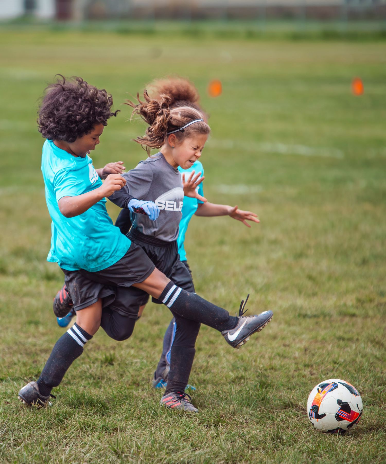 Two young girls compete for a soccer ball during a youth league match on a green grass field.
