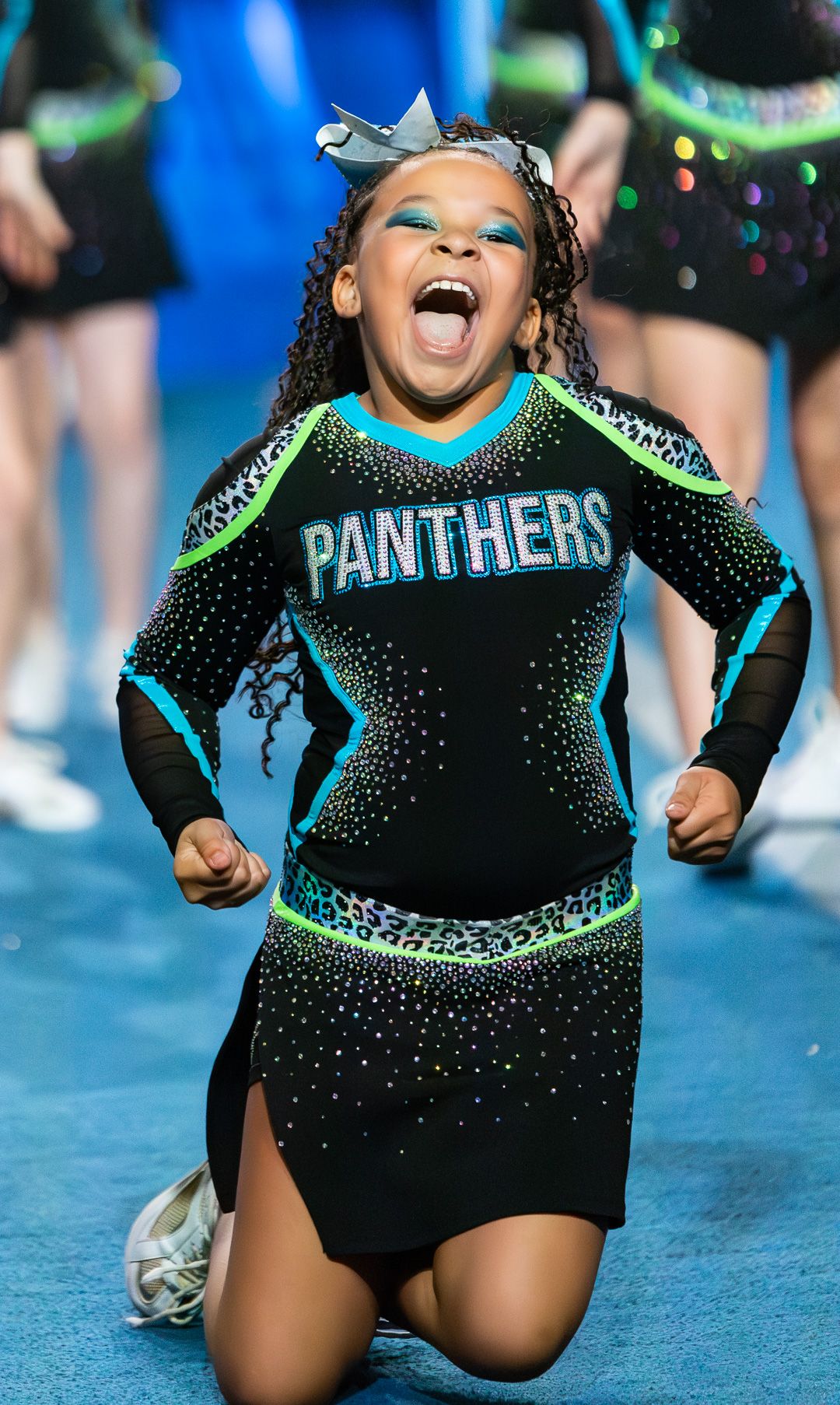 Young girl in Panthers cheerleader uniform cheering enthusiastically during a cheerleading competition.