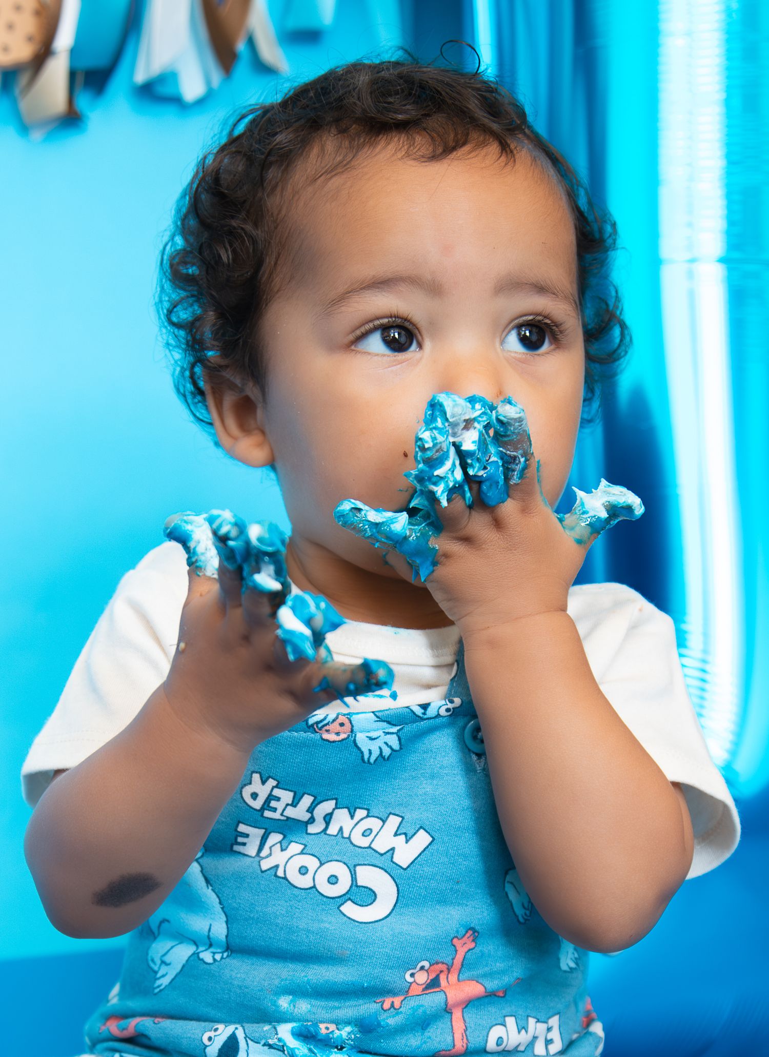 Baby with blue frosting on hands and face wearing a Cookie Monster bib at a first birthday cake smash.