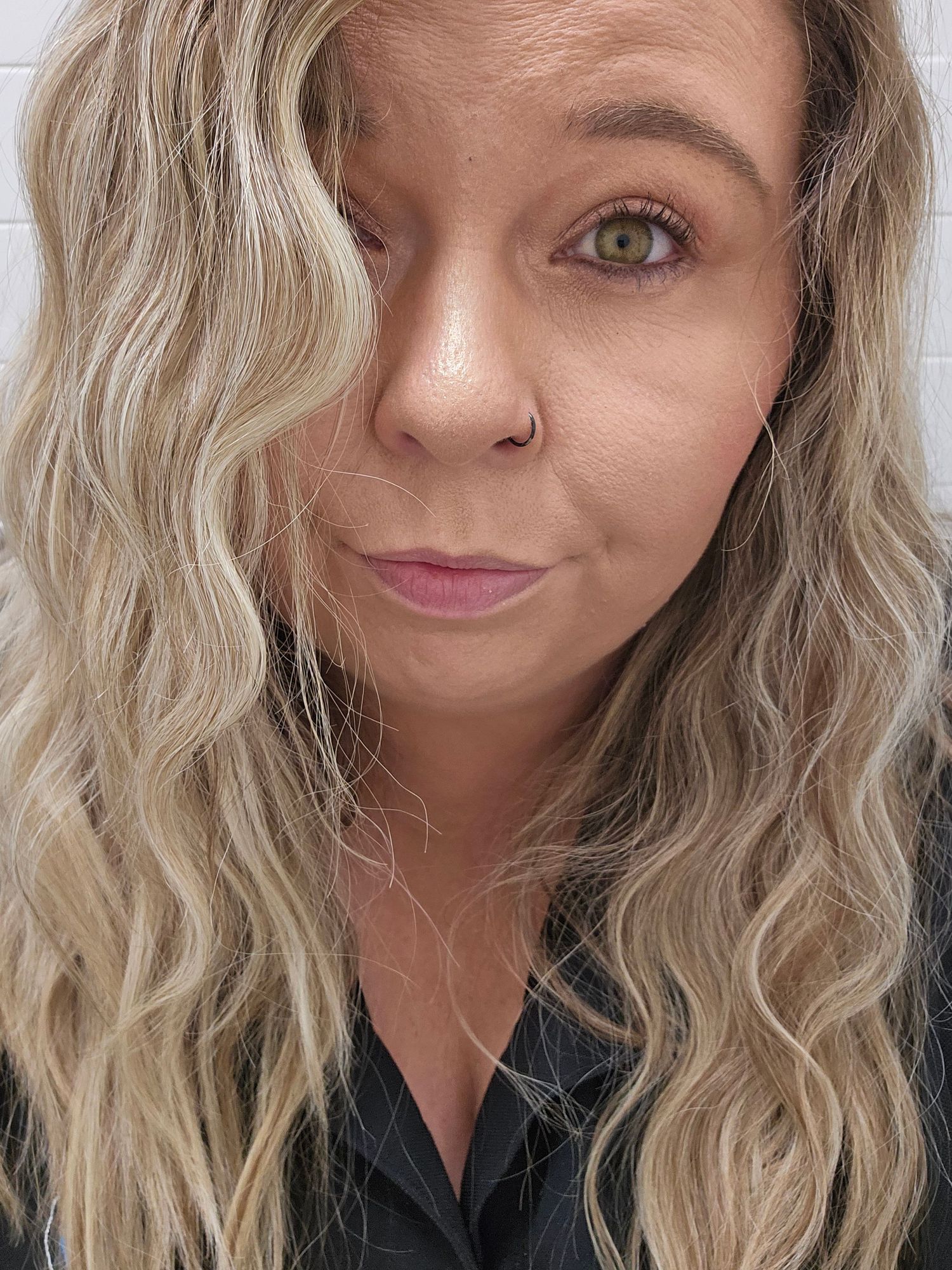 A woman with wavy blonde highlighted hair and green eyes takes a close-up selfie.
