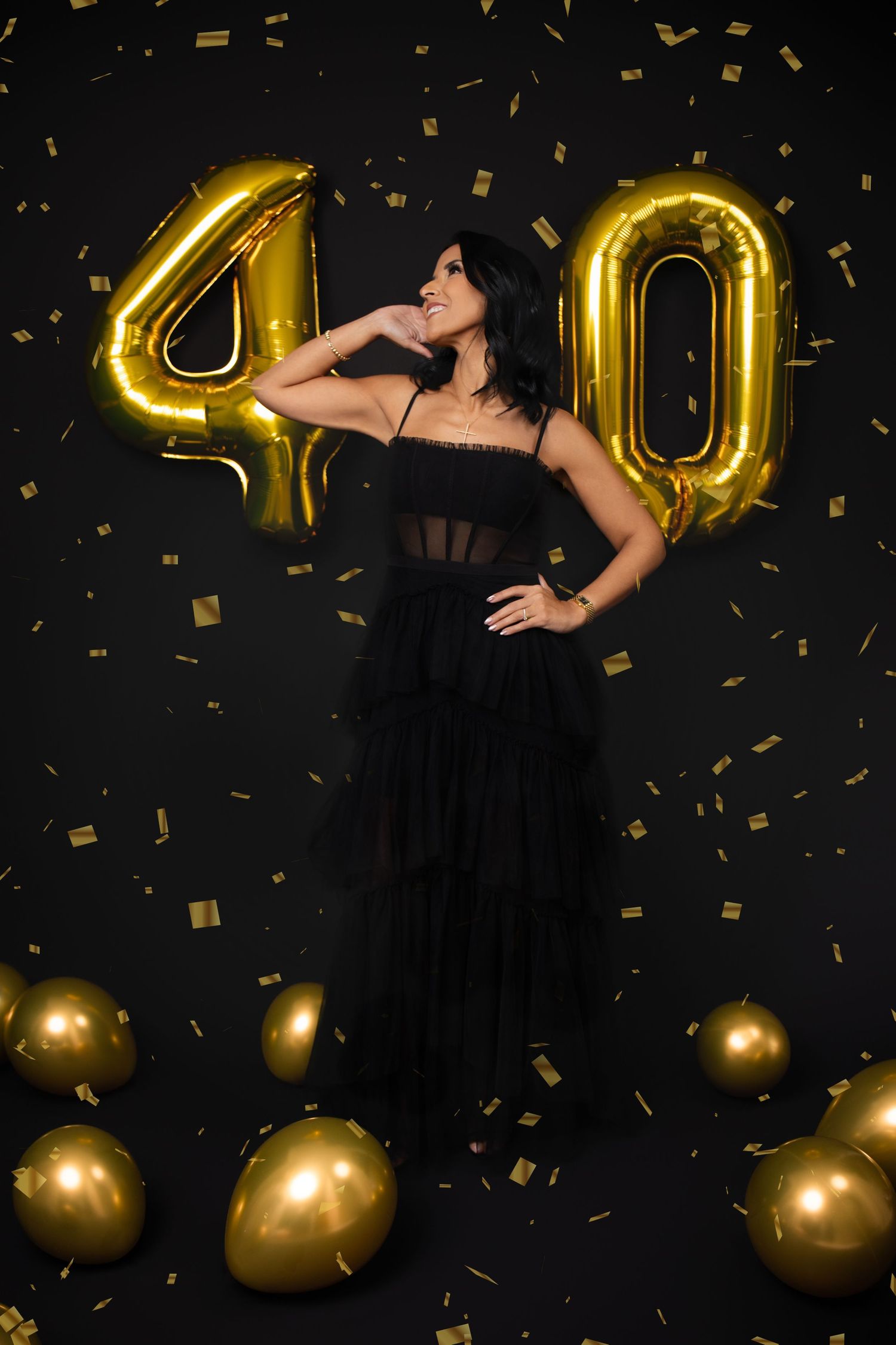 A black and gold 40th birthday celebration setup with large gold number balloons and scattered gold decorations against dark backdrop.