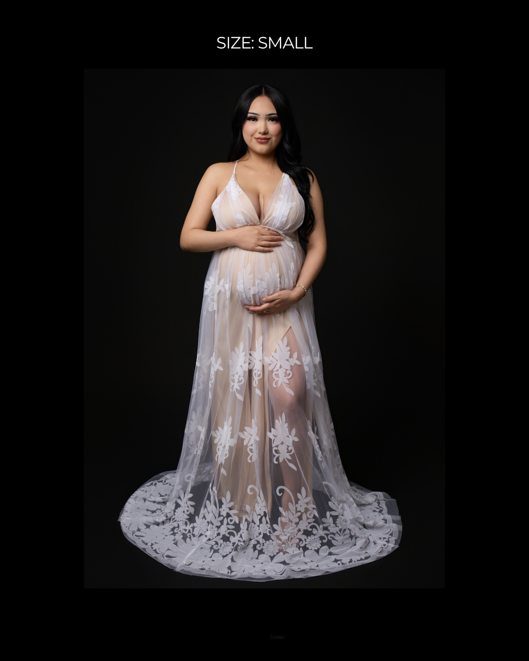 Pregnant woman in size small white lace maternity gown with deep V-neck and floral appliques on dark background.
