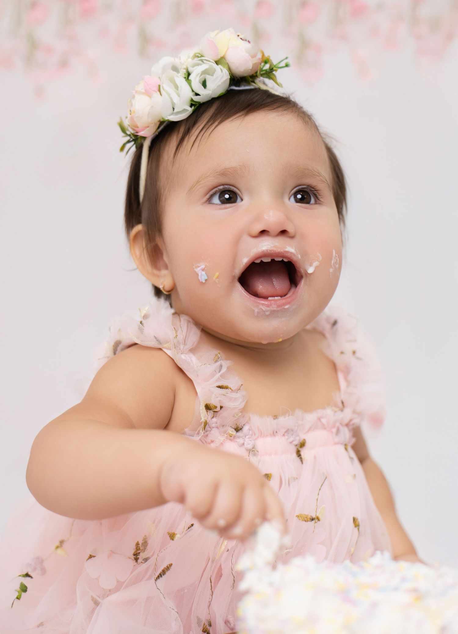A baby wearing a pink tulle dress and floral crown poses during a whimsical photo session with glitter accents.