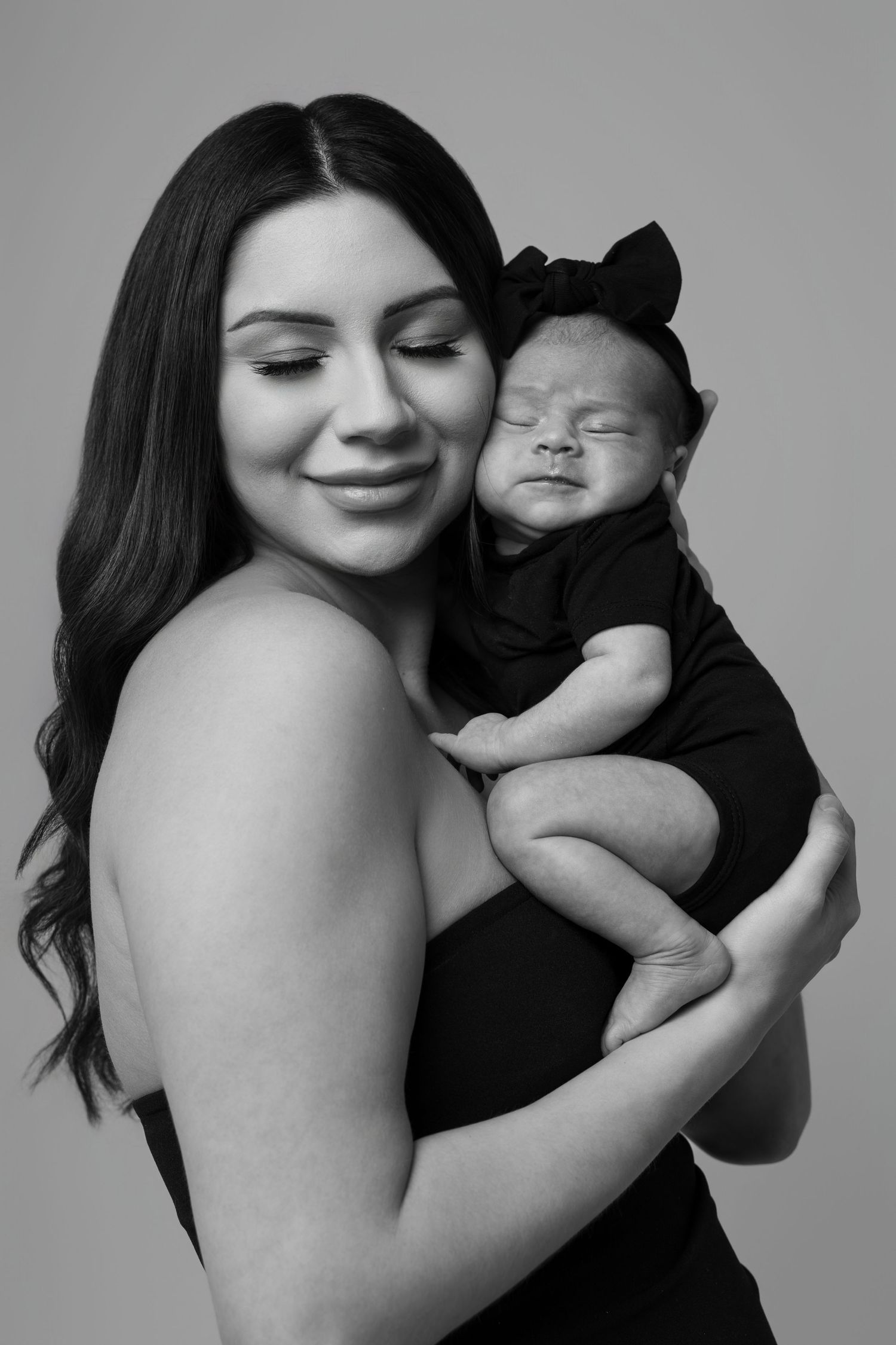 Studio portrait of mother and baby in matching black outfits with bow accessory.