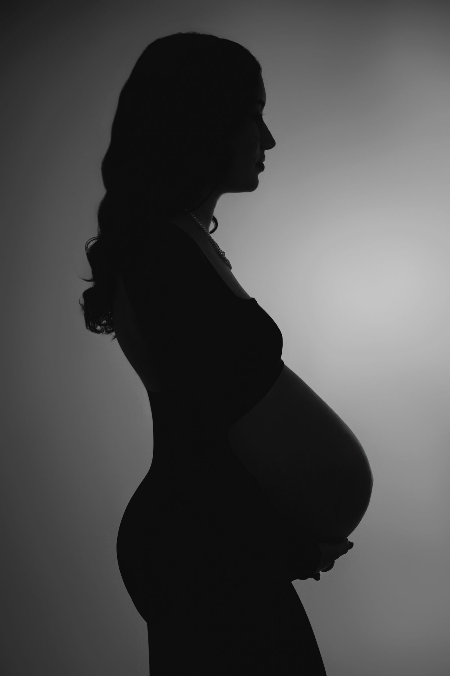 Black and white silhouette of a pregnant woman cradling her baby bump against a soft gradient background.